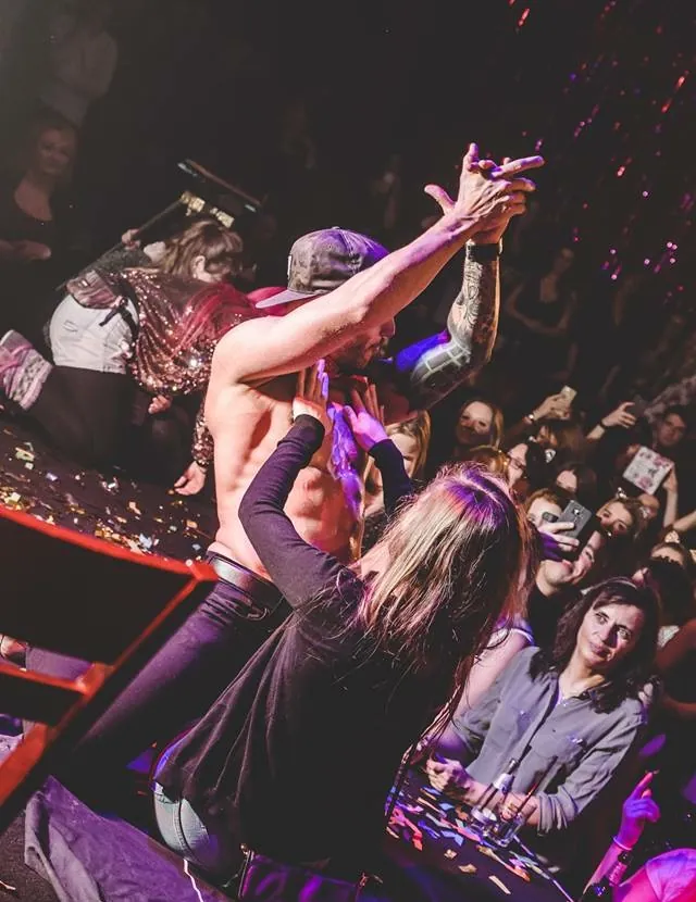 Stripper mit erhobenen Armen im Club, Gäste tanzen und filmen mit